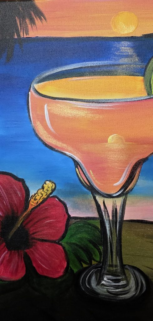 Orange margarita with a lime slice and red hibiscus flower overlooking a tropical sunset